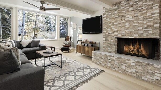 A modern living room with a fireplace, large windows, and a flat-screen TV. - Chateau Snow Unit 202 | Renovated Condo with Great Natural Light, Excellent Location (Aspen)