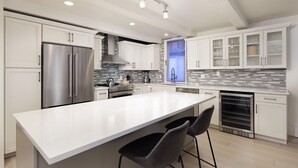 A modern kitchen with white cabinetry, a stainless steel refrigerator, a large island with bar stools, and a built-in oven. - Chateau Snow Unit 202 | Renovated Condo with Great Natural Light, Excellent Location (Aspen)