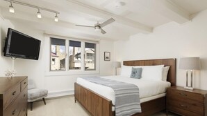 A bedroom with a bed, bedside tables, a TV, and a window. - Chateau Snow Unit 202 | Renovated Condo with Great Natural Light, Excellent Location (Aspen)