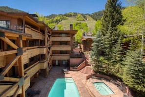 Un edificio in legno a più piani con area piscina, posti a sedere all'aperto e vista su un pendio boscoso.
