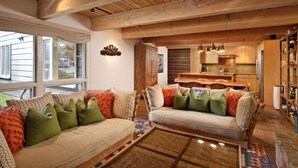A cozy living room with two sofas, a coffee table, and a kitchen area with wooden cabinets and a dining table. - Cottonwoods Unit 1C | Downtown Condo with Upgraded Kitchen & Bathrooms (Aspen)