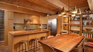 A wooden kitchen with a central island, bar stools, and a dining table. - Cottonwoods Unit 1C | Downtown Condo with Upgraded Kitchen & Bathrooms (Aspen)