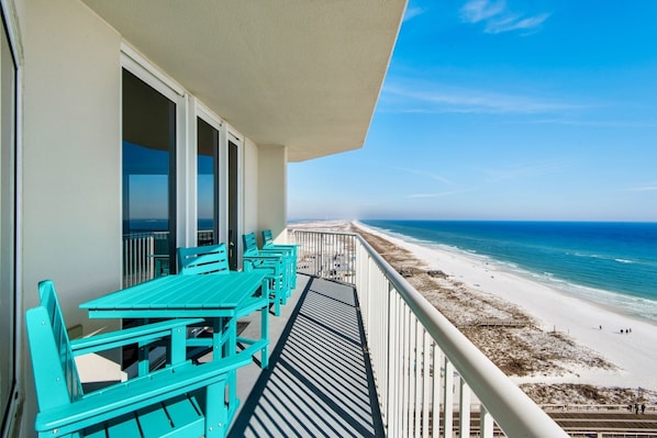 A balcony with turquoise tables and chairs overlooking a beach.