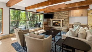 Un salon moderne avec une cheminée en pierre, de grandes fenêtres et des poutres en bois.