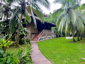 A wooden building with a staircase leading to a covered area, surrounded by lush greenery and a well-maintained lawn. - Ocean Forest Ecolodge Retreat (Drake Bay)
