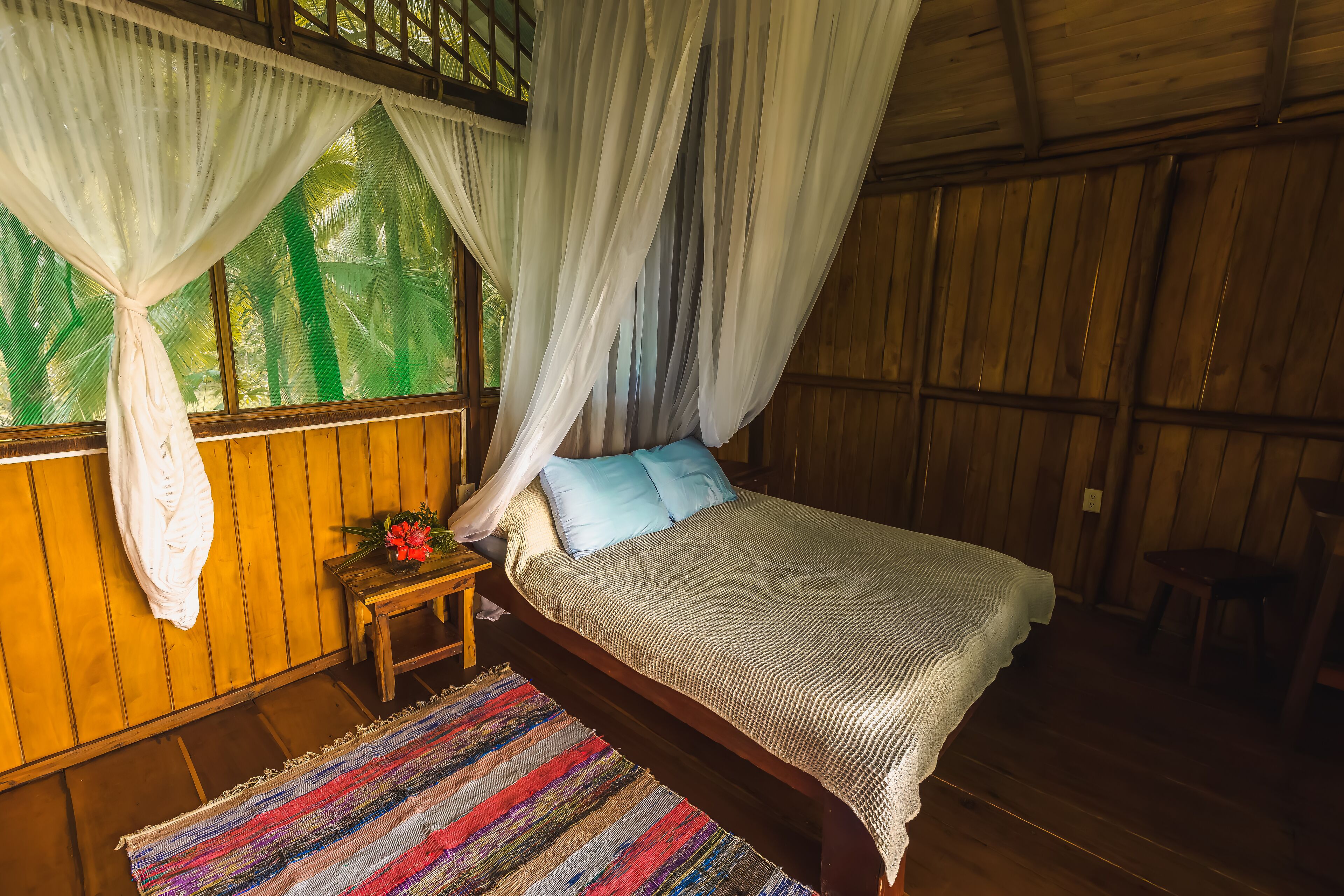 Una habitación de madera con una cama, una mesita de noche y una ventana con cortina.