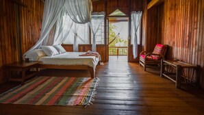 A wooden room with a bed, a chair, and a view through an open door. - Ocean Forest Ecolodge Retreat (Drake Bay)