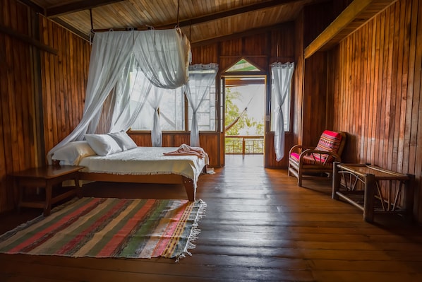 A wooden room with a bed, a chair, and a view through an open door.