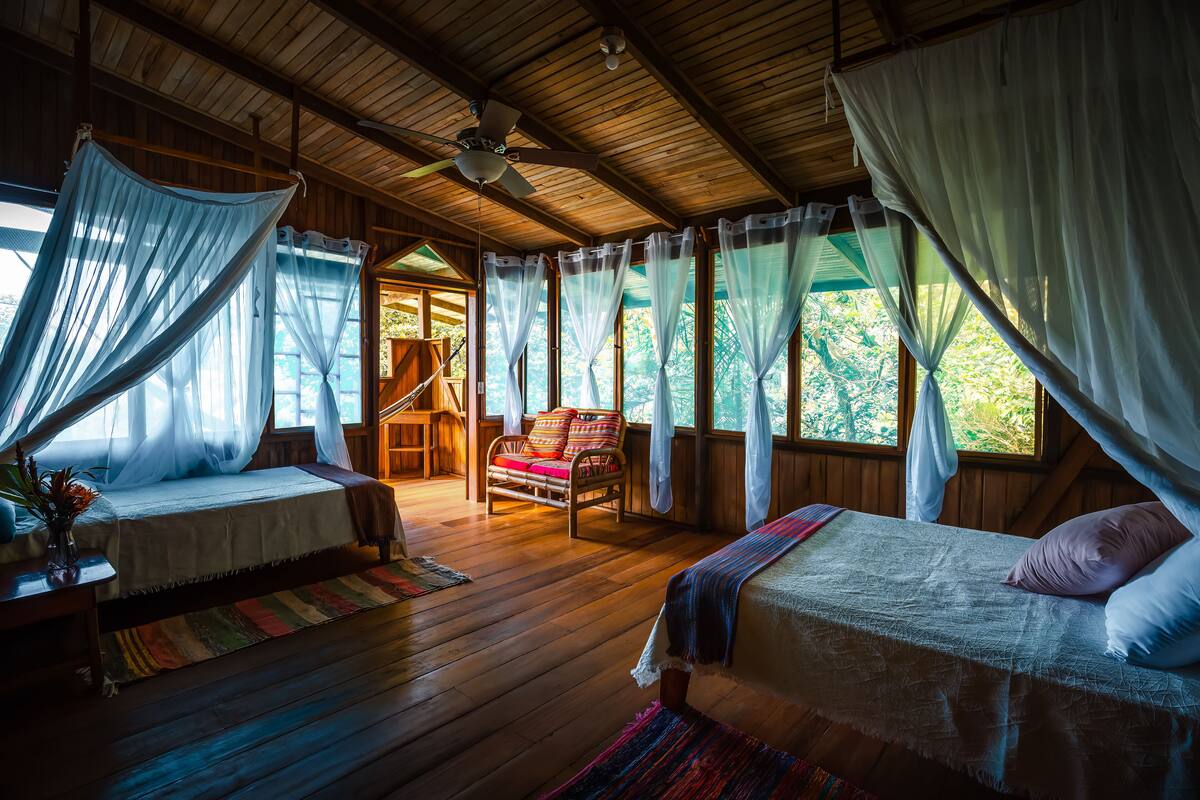 A room with two beds, a wooden ceiling, a ceiling fan, and a view of the outdoors.