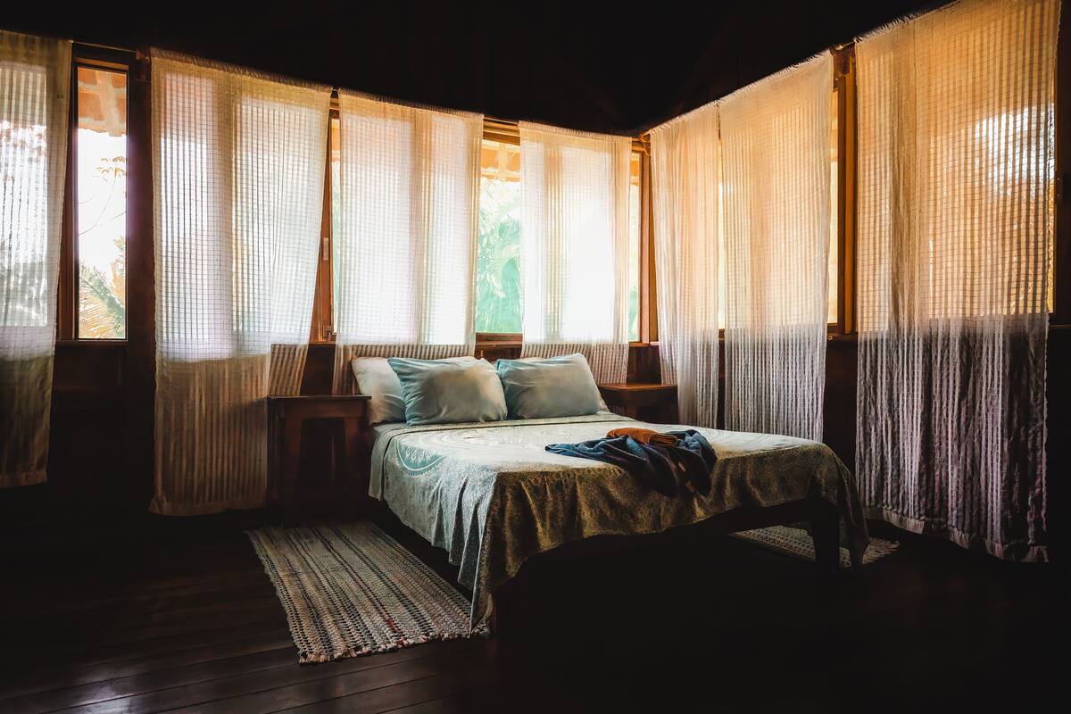 A room with a bed, wooden headboard, and a window with sheer curtains.