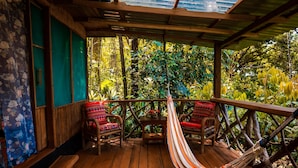 A wooden deck with a hammock, wicker chairs, and a table. - Ocean Forest Ecolodge Retreat (Drake Bay)