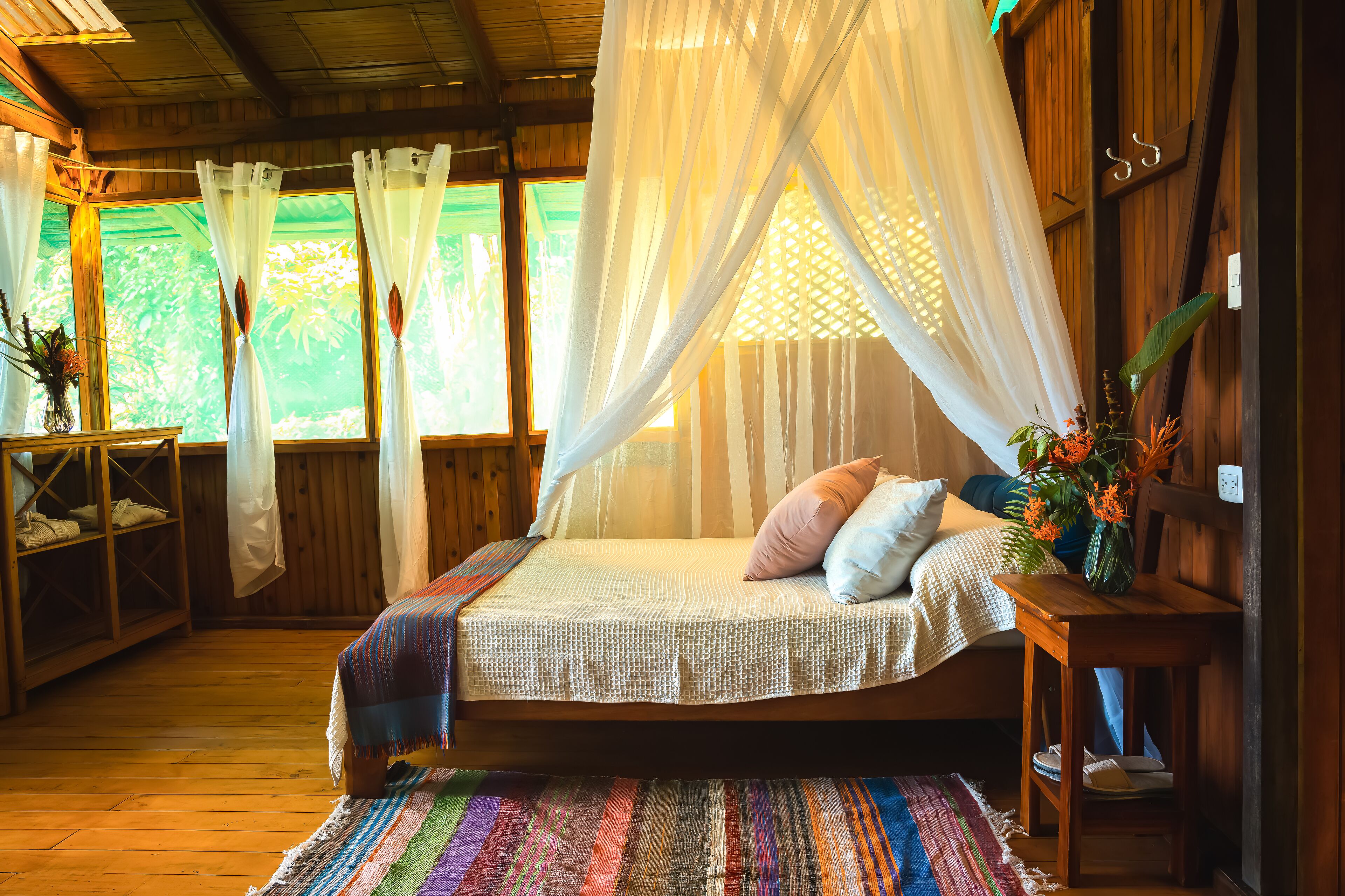 A cozy room with a bed, a wooden wardrobe, a small table with a vase, and a window with curtains.