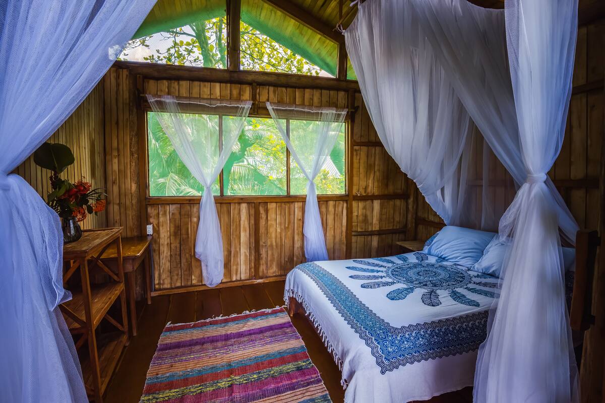 A room with a bed, a wooden desk, and a window with curtains.