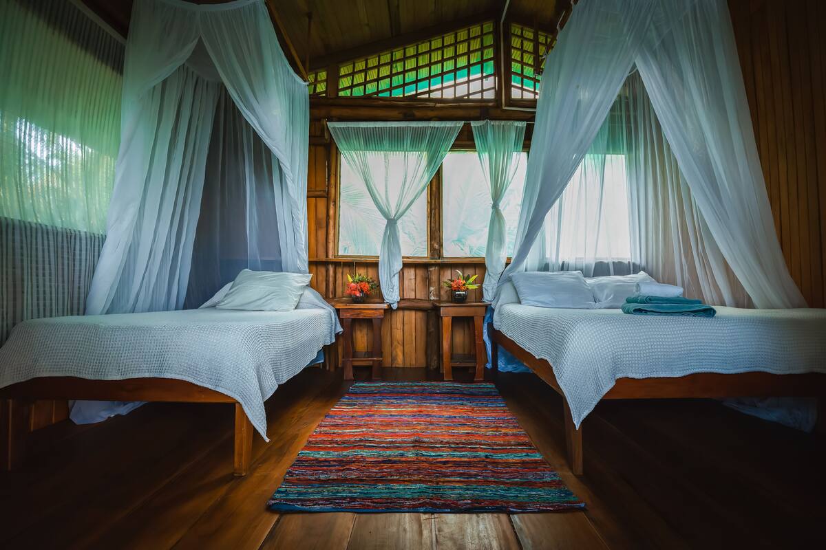 A room with two beds, a wooden floor, and a colorful rug.