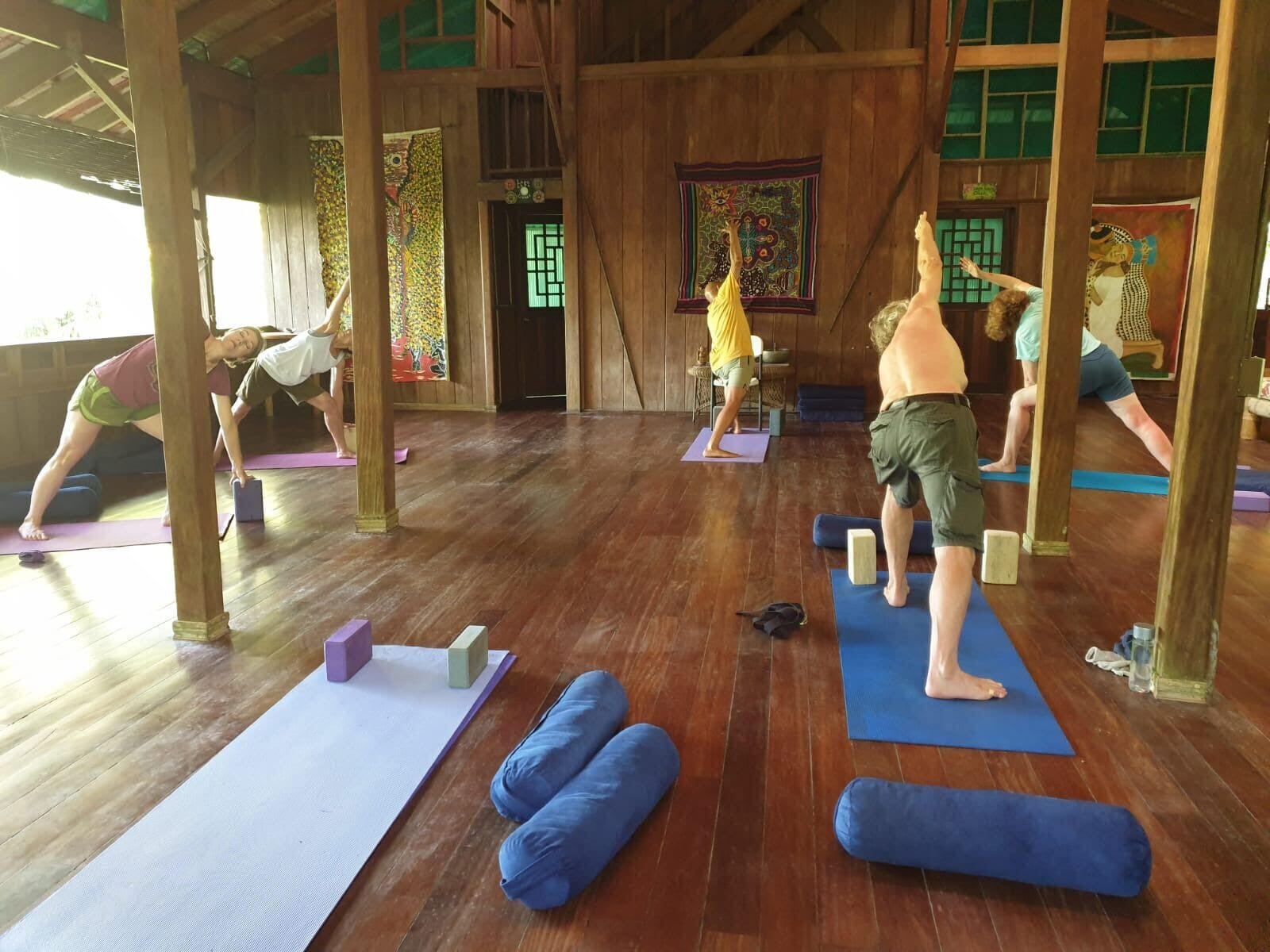 Un cours de yoga dans une pièce en bois, dotée de tatamis et de piliers en bois.