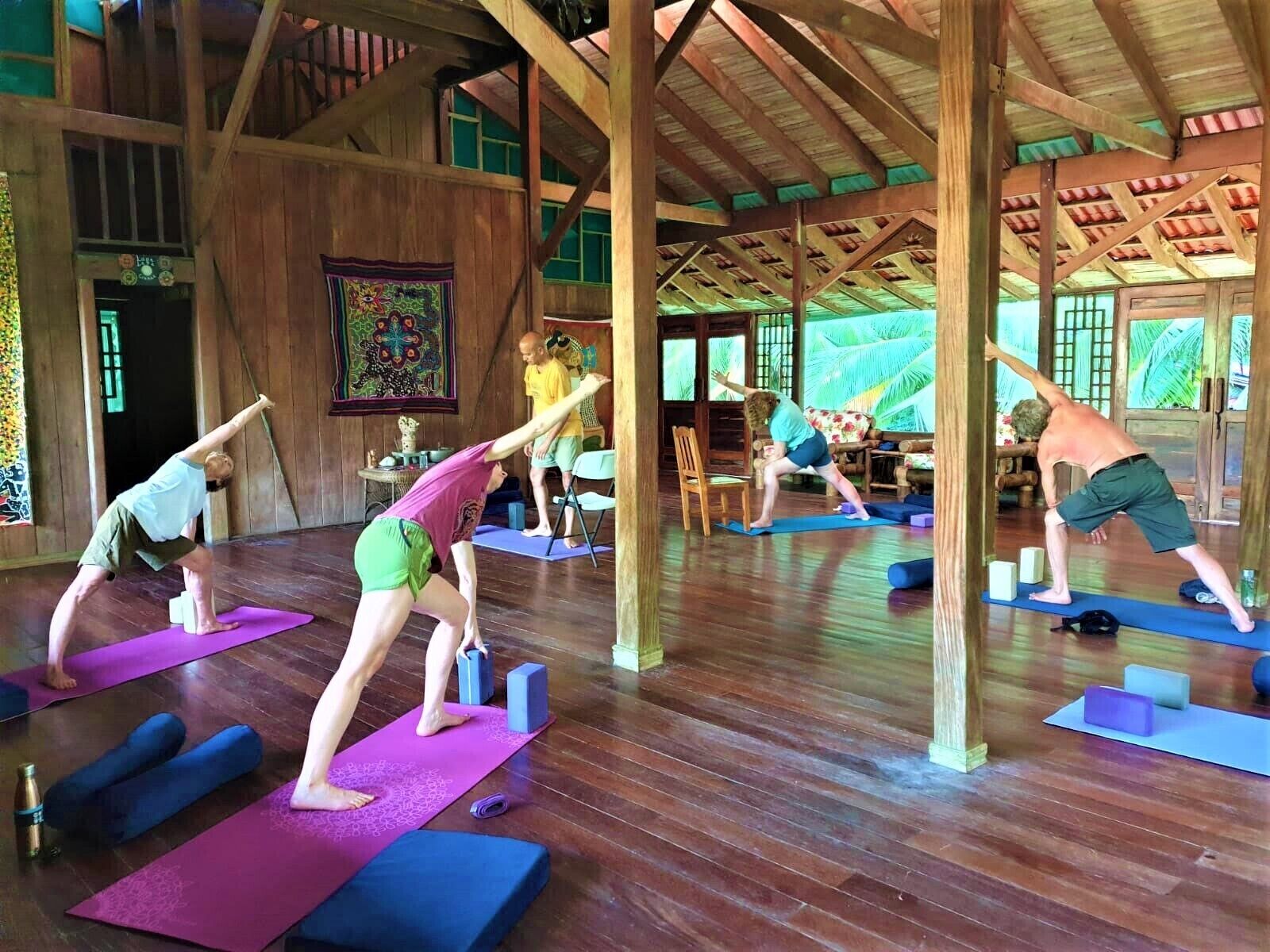Ein Yoga-Studio mit Holzbalken, Holzdielen und großen Fenstern.
