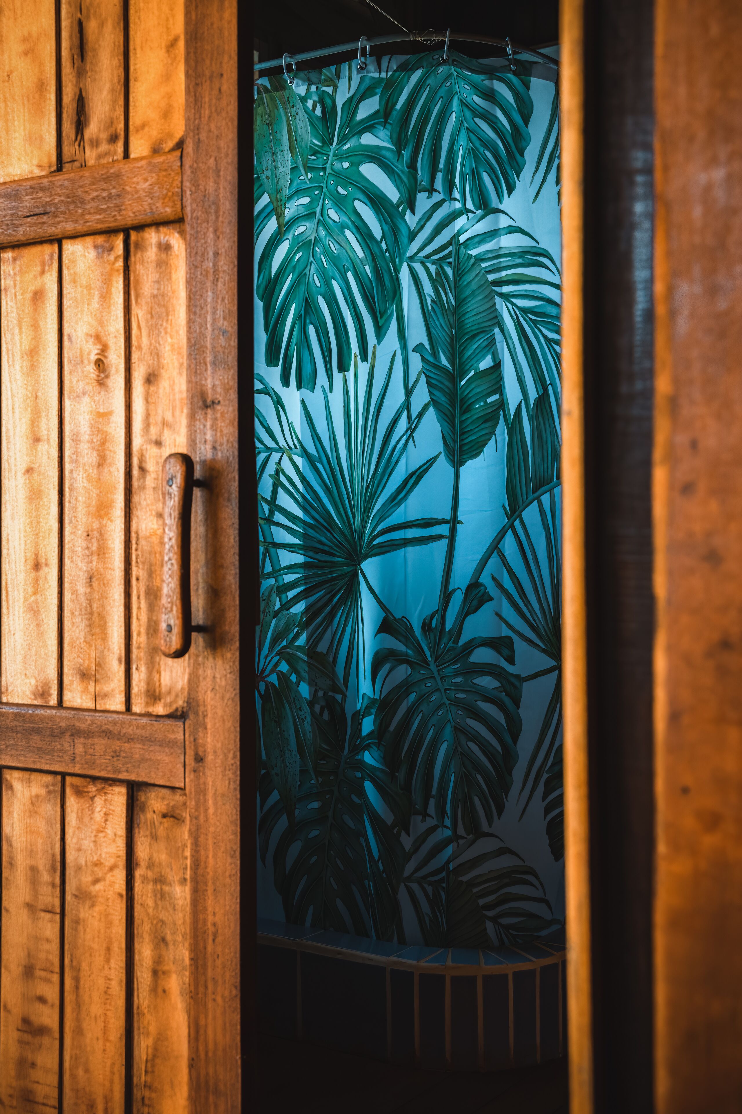 Una puerta de madera con cortina que presenta motivos de hojas tropicales.