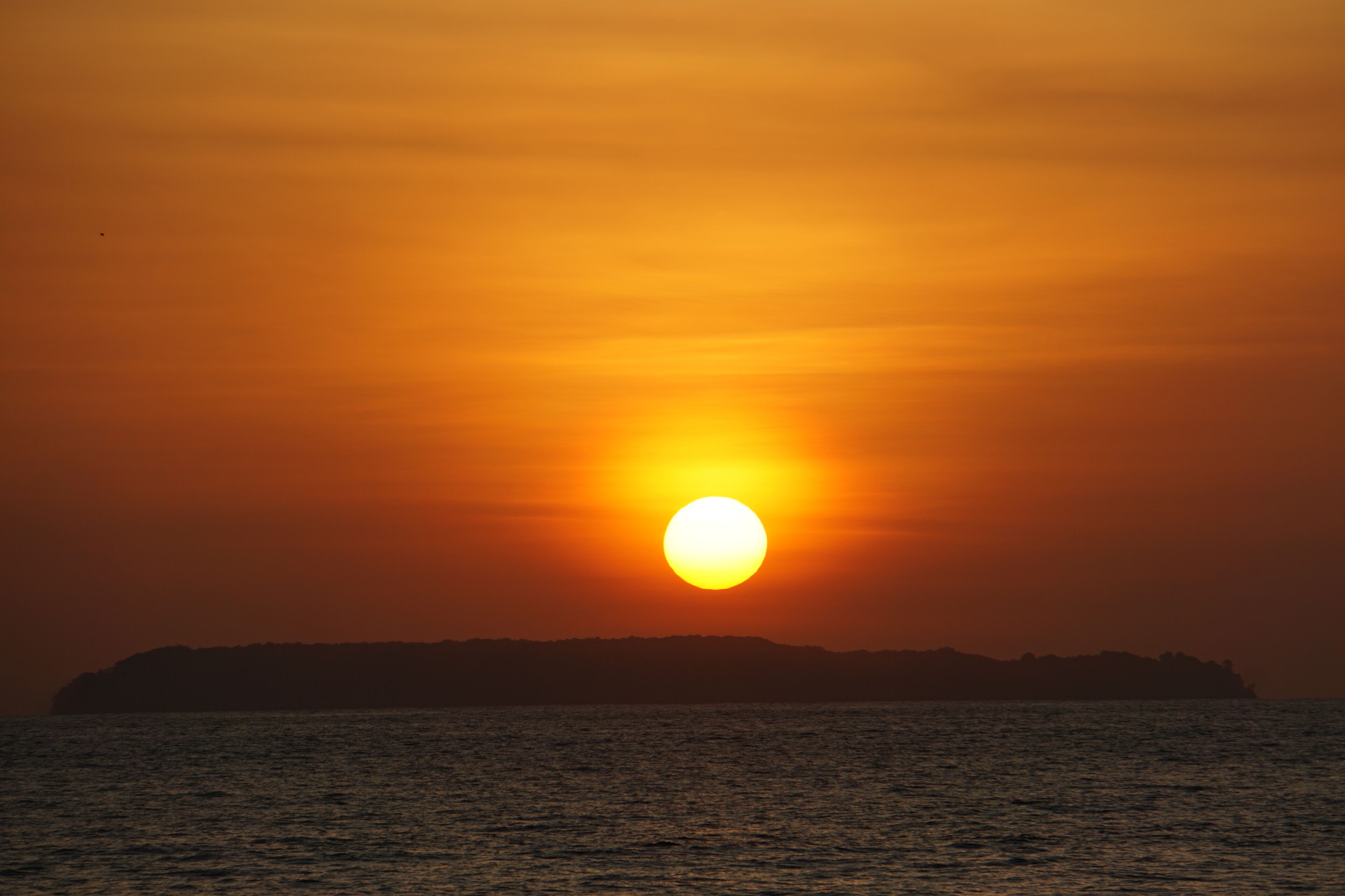 Ein Sonnenuntergang über einem Gewässer, im Hintergrund die Silhouette eines Landabschnitts.