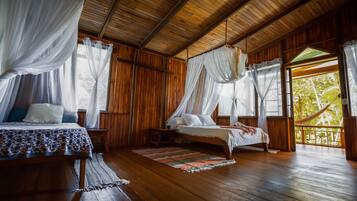 Habitació de fusta amb dos llits, cadascun amb cortina, i una finestra gran amb vista a arbres.