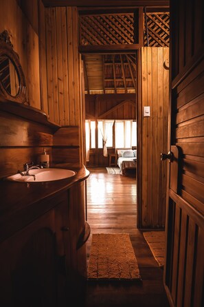 A wooden cabin interior with a wooden door, a sink, and a bed with a window in the background. - Ocean Forest Ecolodge Retreat (Drake Bay)