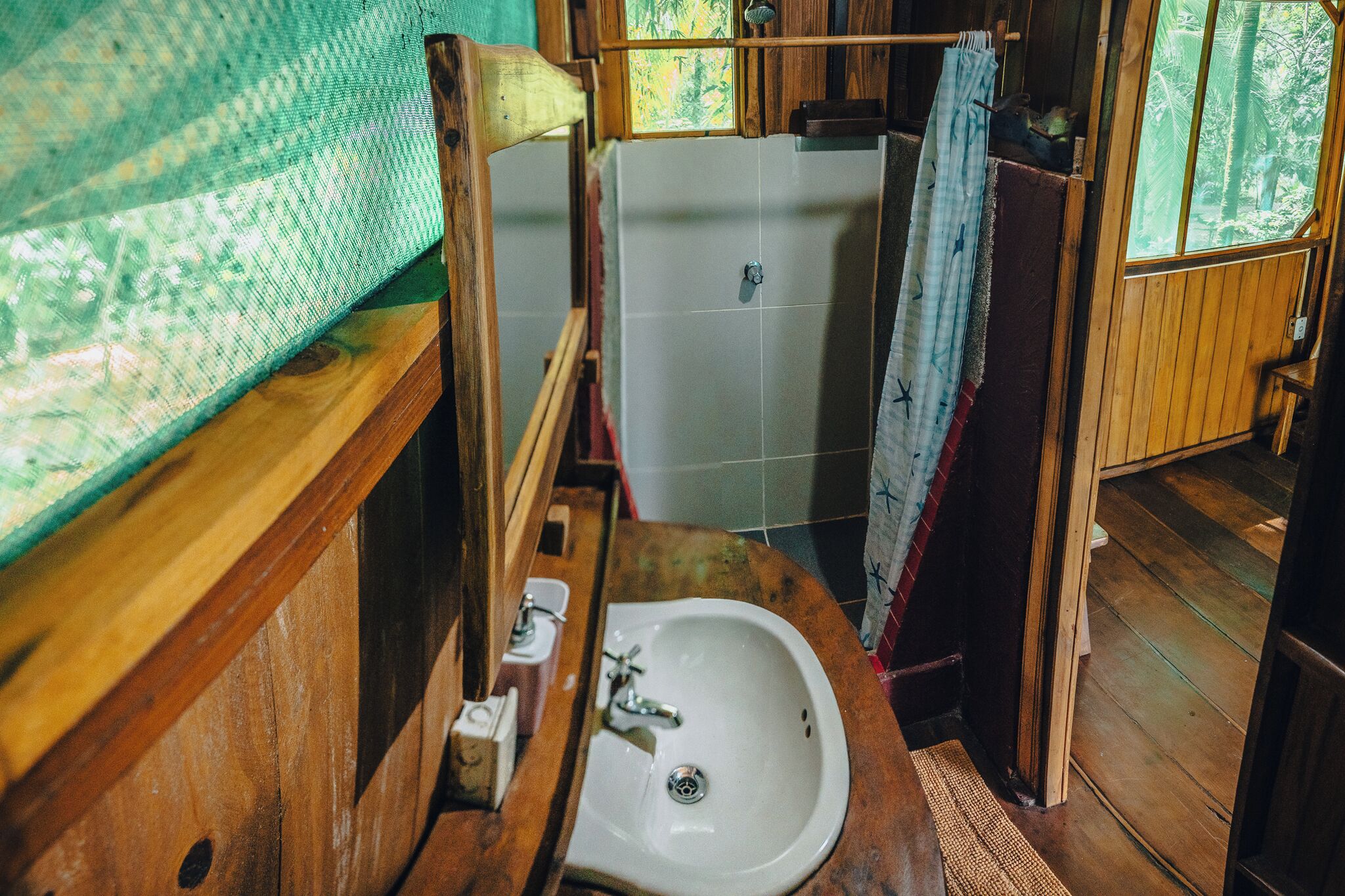 Un baño rústico con un lavabo de madera, zona de ducha y ventana con vistas a zonas verdes.