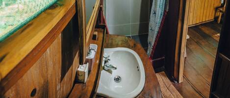 Un baño rústico con un lavabo de madera, zona de ducha y ventana con vistas a zonas verdes.