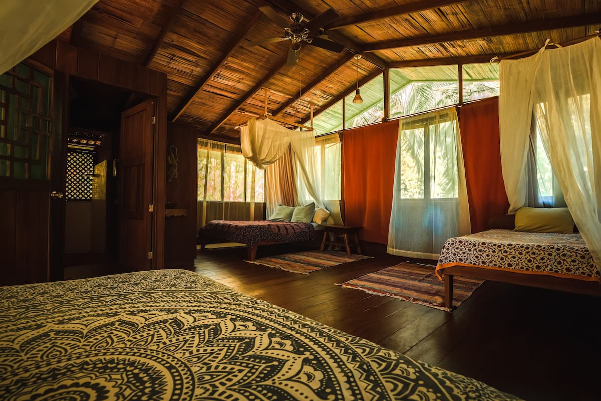 A room with a wooden ceiling, a bed with a patterned bedspread, two bedside tables with lamps, and a window with curtains.