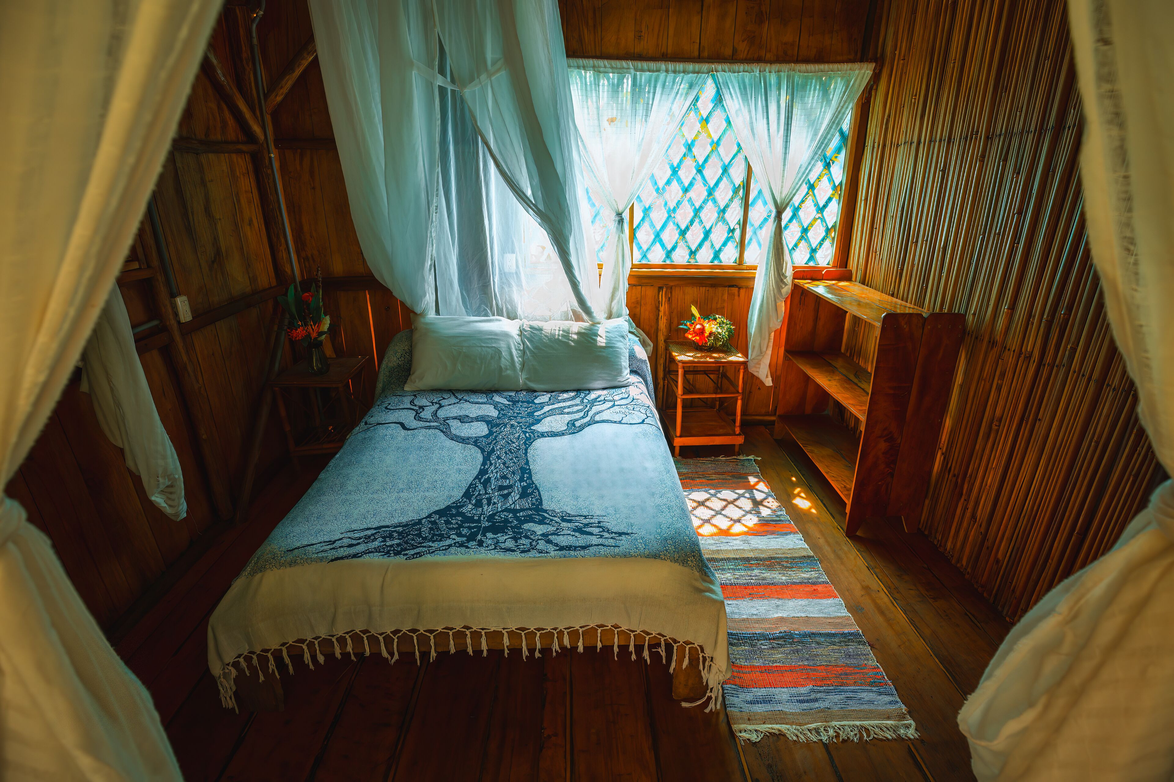 A room with a bed, a small table with a vase, and a bench.