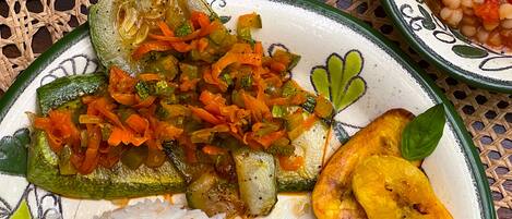 A plate with rice, a stuffed vegetable, a side of beans, and a glass of water on a woven placemat.