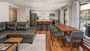 Ein modernes Wohnzimmer mit einem Ecksofa, einem Couchtisch aus Holz und einem Essbereich mit Holztisch und -stühlen.