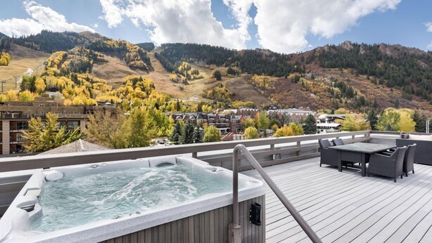 Eine Dachterrasse mit Whirlpool, Gartenmöbeln und Blick auf eine Stadt und Berge.