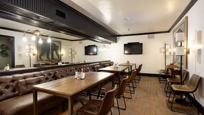 Un restaurante con una barra alargada, asientos tipo banca de cuero y un televisor colgado en la pared.