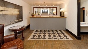 Un vestíbulo de hotel con una recepción, un cuadro abstracto de gran tamaño, un tapete estampado y un sillón de cuero.