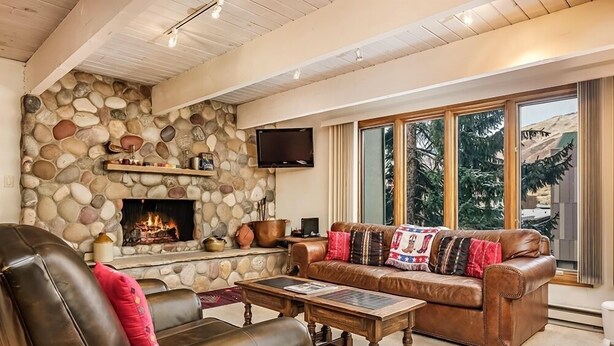 A cozy living room with a stone fireplace, leather sofas, and a large window with a view of trees.