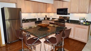 A modern kitchen with a stainless steel refrigerator, a microwave, a stove, and a large island with bar stools.