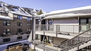 Un edificio de varios pisos con balcones, una escalera y un automóvil estacionado adelante.