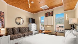 A hotel room with a bed, a seating area with a TV, a dining table, and a view of the outside. - Independence Square 305 | Remodeled, 3rd Floor Hotel Room in Aspen's Best Location (Aspen)