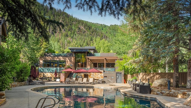 Zona de piscina con terraza de piedra, sillas de descanso y sombrillas, rodeada de bosque denso y montañas al fondo.