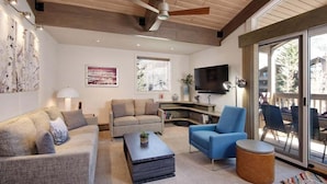 Una sala de estar moderna con un ventilador de techo, un televisor de pantalla plana y un amplio ventanal corredero al exterior.