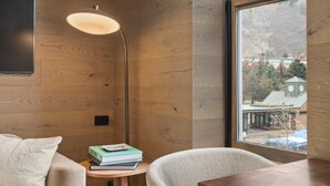 A modern room with wooden walls, a large window, a sofa, a table, and a floor lamp. - Independence Square 301 | Great Hotel Room with Excellent Location & Rooftop Hot Tub (Aspen)