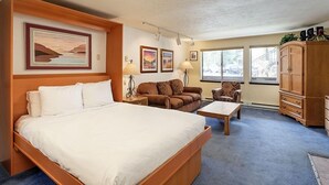 A hotel room with a large bed, a sofa, a chair, a wooden cabinet, and a window with a view of the outside.