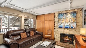 Una sala de estar acogedora con un sofá de cuero, una chimenea y una pared de piedra.