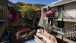 Un edificio a più piani con piscina, balconi decorati con fioriere e vista su un paesaggio collinare.