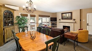 Un salón espacioso con una mesa de comedor de madera, sillas verdes, un sofá de cuero marrón y un sillón amarillo, además de una chimenea.