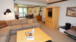 A living room with a sofa, coffee table, TV stand, and dining area. - Riverview Unit 8 | All the Essentials Riverside Condo with Access to Pool & Hot Tub (Aspen)