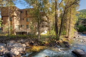 Un immeuble à plusieurs étages doté de balcons, avec un ruisseau en contrebas et des arbres.