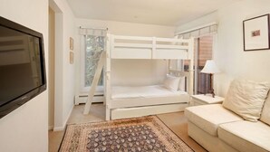 A bedroom with bunk beds, a television, a sofa, a lamp, and a patterned rug. - Old Hundred Unit 102 | Townhouse with Treetop Views & Excellent Location, 3 Blocks to Ski Slopes (Aspen)