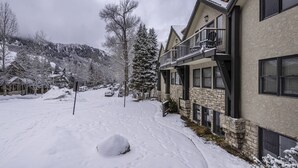 A snow-covered residential area with houses featuring stone and brick exteriors, a balcony, and a clear view of the surrounding snowy landscape.