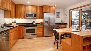 A modern kitchen with wooden cabinets, stainless steel appliances, and a dining area with a wooden table and chairs.