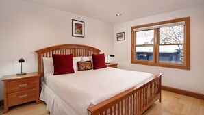 A bedroom with a wooden bed frame, a nightstand with drawers, a bedside table, and a window with a view of a snowy landscape.